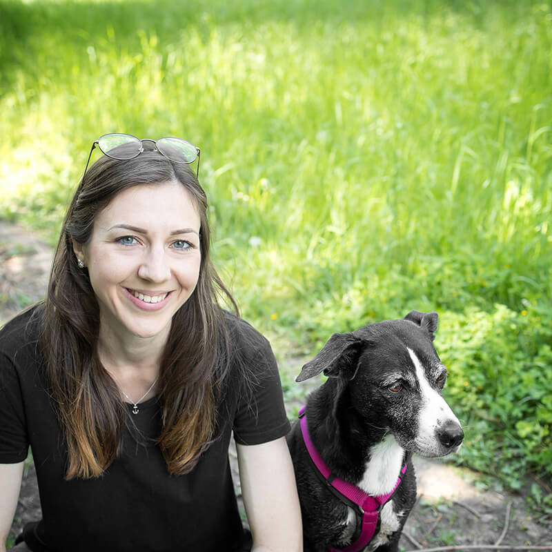 Hundeschule Heidelberg: Hundetrainerin Julie sitzt mit ihrem Hund Bonnie auf einem Weg und lächelt in die Kamera.
