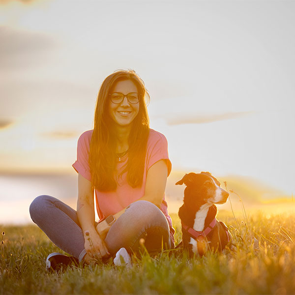 Hundeschule Heidelberg: Hundetrainerin Julie sitzt mit ihrem Hund Bonnie auf einem Weg und lächelt in die Kamera.